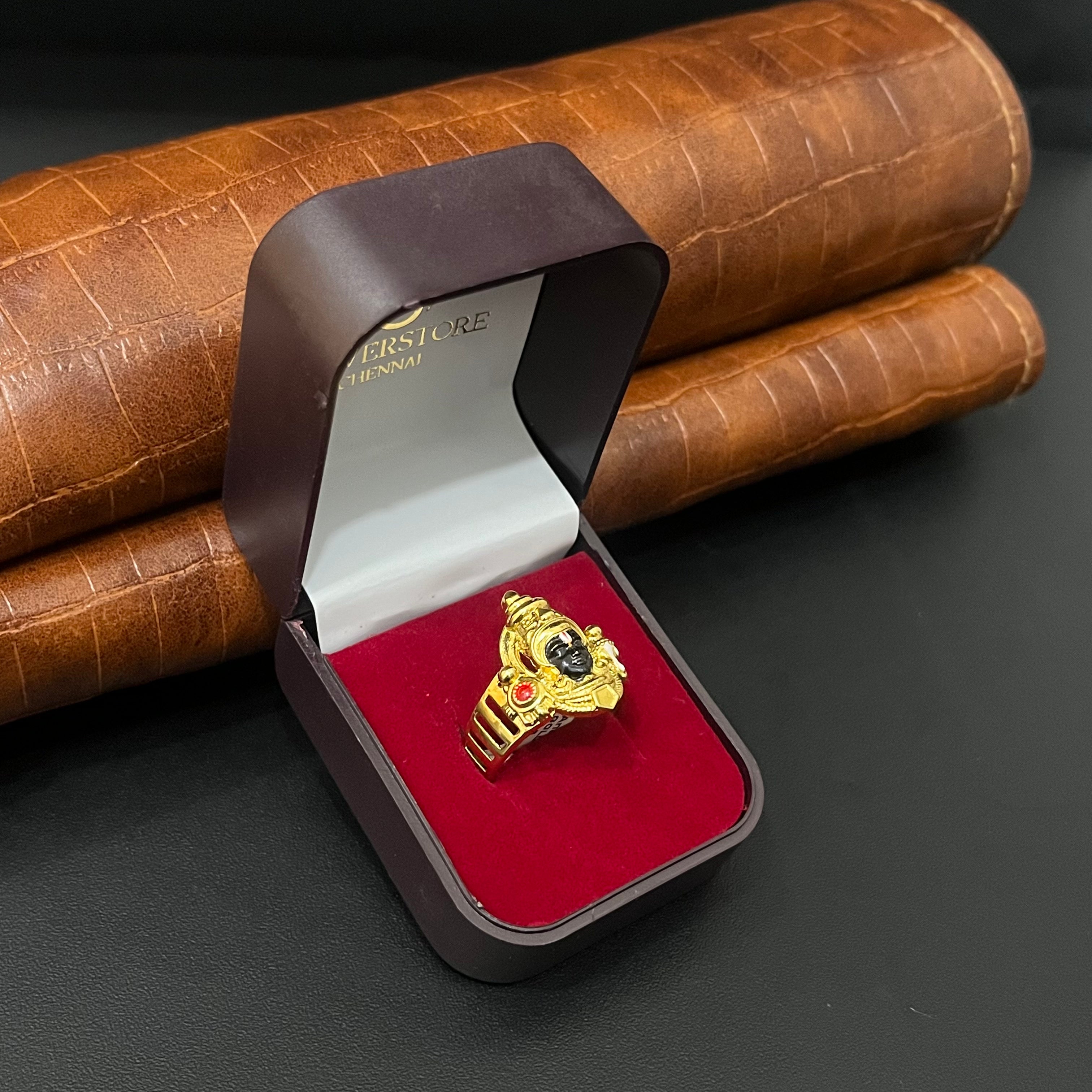 A gold ring displayed inside an open dark brown jewelry box with a red velvet lining, set against a brown textured leather background.